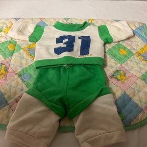 May include: Green and white tracksuit with a white long-sleeved shirt with green trim and the number 31 in blue on the front. The trousers are green with white cuffs.