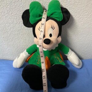 Puede incluir: Mu&ntilde;eca de peluche de Minnie Mouse con vestido y lazo verdes. La mu&ntilde;eca tiene orejas negras, cara blanca y zapatos negros. La mu&ntilde;eca mide aproximadamente 35,5 cm de altura.