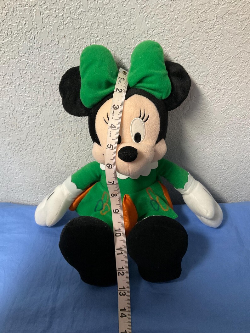Puede incluir: Mu&ntilde;eca de peluche de Minnie Mouse con vestido y lazo verdes. La mu&ntilde;eca tiene orejas negras, cara blanca y zapatos negros. La mu&ntilde;eca mide aproximadamente 35,5 cm de altura.