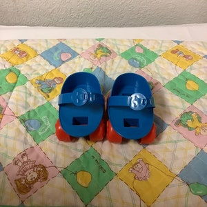 May include: A pair of blue and orange toy roller skates with a strap and buckle on each skate.