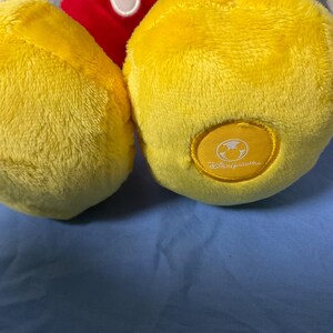 Pode incluir: Um brinquedo de pel&uacute;cia amarelo Mickey Mouse com uma camisa vermelha e contornos pretos. O brinquedo tem uma etiqueta amarela no p&eacute; direito com o logotipo da Disney.