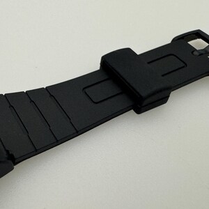 May include: Black watch strap with a buckle closure. The strap is made of a textured rubber material.