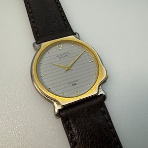 Può includere: Un orologio da polso Bulova Quartz Longchamp 920 in oro e argento con un cinturino in pelle marrone.