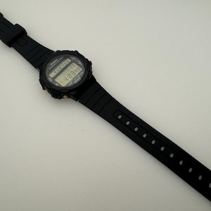 May include: A black digital wristwatch with a black resin band. The watch face displays the time, date, and other functions.
