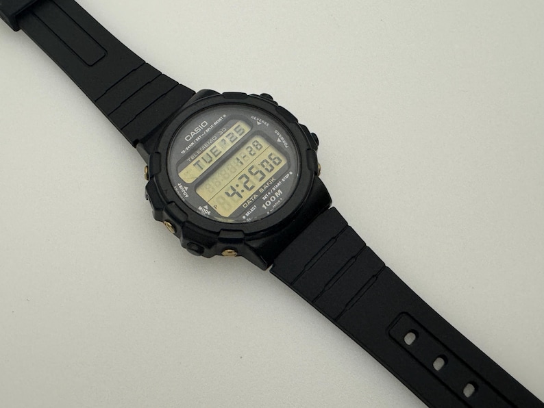 May include: Black Casio digital wristwatch with a black band and gold accents. The watch face displays the time, date, and day of the week. The watch is water resistant to 100 meters.