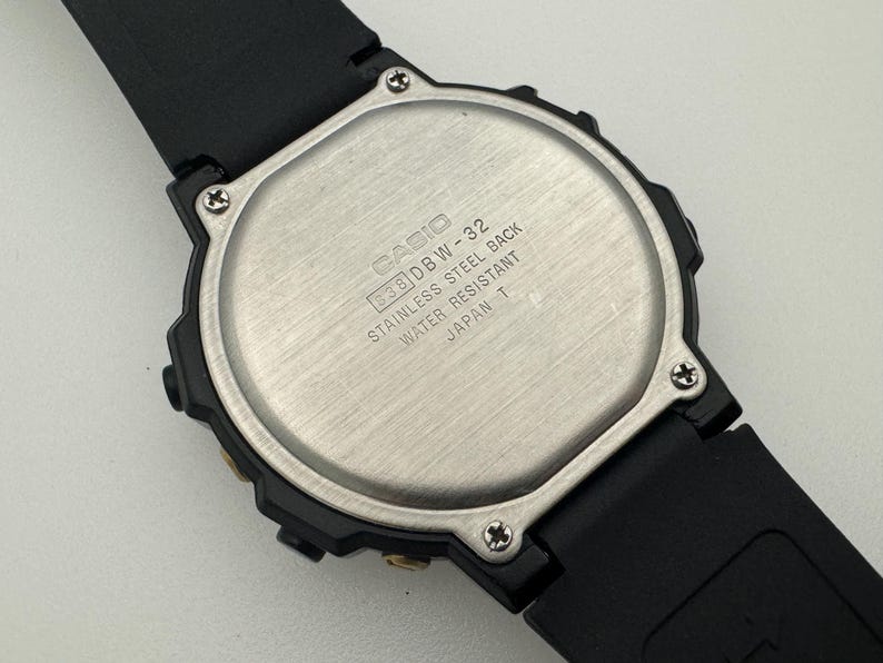 May include: Black Casio wristwatch with a silver back. The back of the watch has the text "CASIO DBW-32 STAINLESS STEEL BACK WATER RESISTANT JAPAN T".