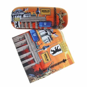 Könnte beinhalten: Ein orangefarbenes Brillenetui und ein Reinigungstuch mit Berliner Wahrzeichen. Das Etui und das Tuch zeigen Bilder des Brandenburger Tors, des Berliner Fernsehturms und des Berliner Bärensymbols mit den Texten "Berlin" und "Alexanderplatz".