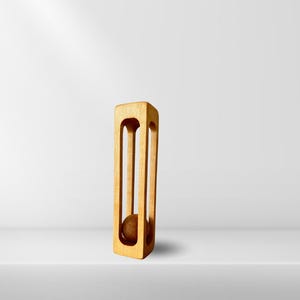 Puede incluir: Una escultura de madera con una bola dentro de un marco cuadrado. La escultura está hecha de madera marrón claro y tiene un acabado liso.