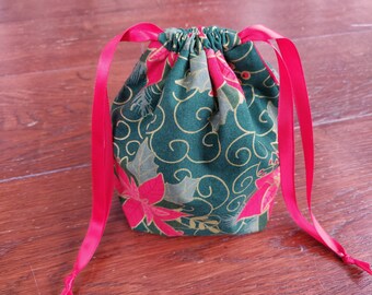 Pode incluir: Uma bolsa de cordão verde com um padrão floral e detalhes dourados. A bolsa tem laços de fita vermelha.