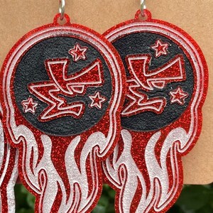 May include: Red and white glitter earrings with a black circle containing a red stylized letter "Z" and white stars. The earrings are shaped like flames.