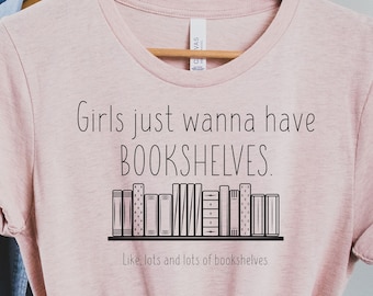 May include: A pink t-shirt with the text "Girls just wanna have BOOKSHELVES. Like, lots and lots of bookshelves" and a graphic of a bookshelf with books on it.