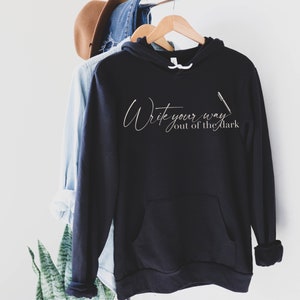 May include: Black hooded sweatshirt with the text "Write your way out of the dark" in white script with a pen graphic.
