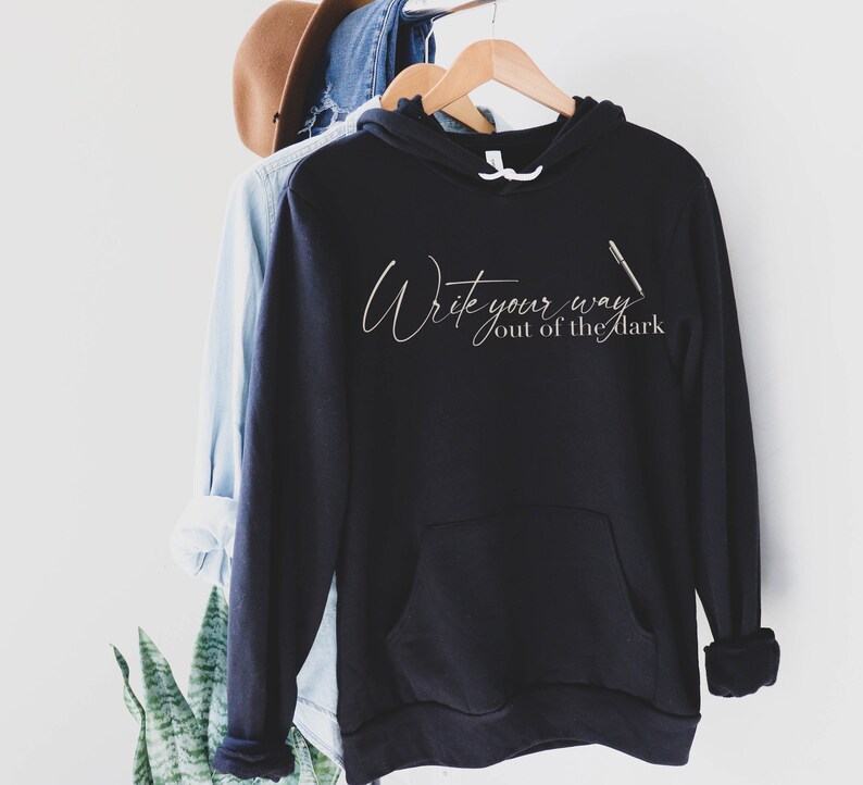 May include: Black hooded sweatshirt with the text "Write your way out of the dark" in white script with a pen graphic.