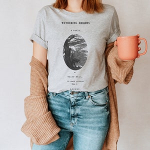 May include: A gray t-shirt with a black and white illustration of a tree and a figure. The text "Wuthering Heights" is printed on the shirt, along with the words "A Novel" and "Ellis Bell".