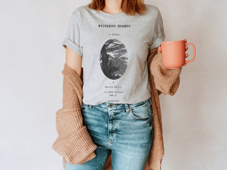 May include: A gray t-shirt with a black and white illustration of a tree and a figure. The text "Wuthering Heights" is printed on the shirt, along with the words "A Novel" and "Ellis Bell".