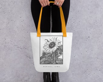 Peut inclure: Sac fourre-tout blanc avec des poignées jaunes illustrant un tournesol en noir et blanc avec le texte "MERIDEL, IOWA" imprimé en dessous.