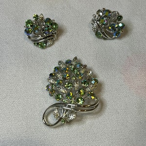 May include: A set of three vintage jewelry pieces featuring a silver tone design with green iridescent rhinestones. The set includes a brooch, a pair of earrings, and a smaller brooch.