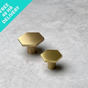 May include: Two gold hexagonal cabinet knobs with a brushed finish. The larger knob is in the background and the smaller knob is in the foreground.