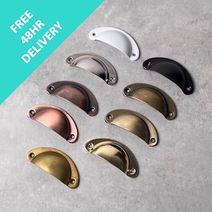 May include: An assortment of eight cup pull cabinet handles in various colours, including white, silver, black, copper, bronze, and gold. The handles are displayed on a grey surface. Text in the top left corner reads "FREE 48HR DELIVERY."