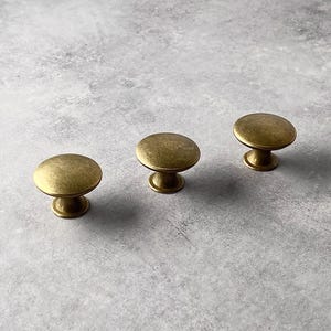 May include: Three gold-toned cabinet knobs with a round, slightly domed top and a short, cylindrical base.