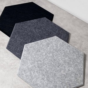 May include: Three hexagonal acoustic panels in different shades of grey. The panels are made of a textured fabric and are designed to absorb sound.