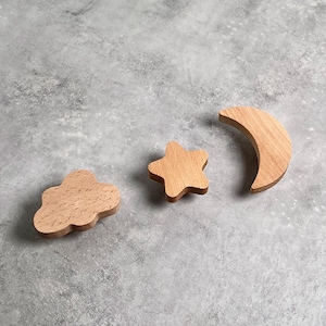 May include: Three wooden shapes, a cloud, a star, and a crescent moon, are arranged on a grey textured surface.