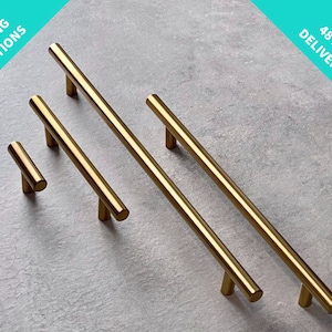 May include: Four gold cabinet pulls in different sizes. The pulls are made of metal and have a brushed finish. The pulls are arranged in a row from smallest to largest.