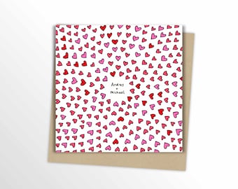 May include: A square greeting card with a pattern of red and pink hearts on a white background. The card includes the names "Andres + Michael" in the center. The card is on a brown envelope.
