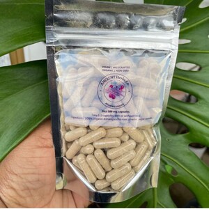 May include: A silver pouch with a clear plastic window showing brown capsules. The pouch is labeled "ANCIENT Herbs Co. Ashwagandha 90ct 500 mg capsules Vegan | Wildcrafted Organic | Non GMO Take 1-2 capsules with or without food 100% Organic Ashwagandha root powder, vegan capsules"