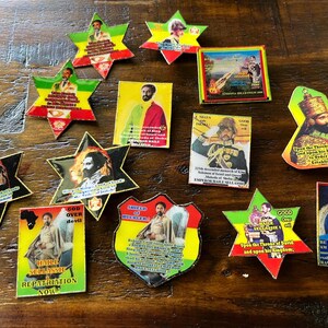May include: A collection of colorful, star-shaped and rectangular stickers and pins featuring portraits of historical figures and religious imagery. The items are arranged on a wooden surface, showcasing a variety of designs and text.