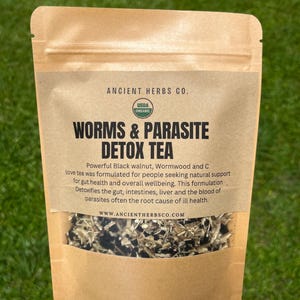 May include: A brown paper bag of "Worms & Parasite Detox Tea" from Ancient Herbs Co. The bag has a clear window showing the tea leaves. Text on the label includes "USDA Organic" and a description of the tea's benefits.