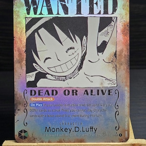 May include: A holographic trading card featuring a smiling cartoon character with the text "WANTED" at the top. The card reads "DEAD OR ALIVE" and includes game instructions and the character's name, Monkey.D.Luffy.
