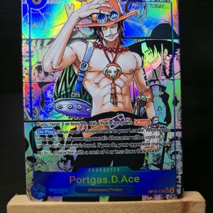 May include: A holographic trading card featuring the character Portgas D. Ace from the anime series One Piece. Ace is depicted shirtless, wearing an orange hat and necklace. The card has a blue and purple background with text that includes "6", "7,000", and "Rush".