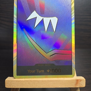 May include: A holographic trading card with a white abstract design and the text "Your Turn +1000".