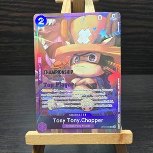 May include: A collectible trading card featuring Tony Tony.Chopper from the One Piece series. The card has a purple and gold holographic design with the text "CHAMPIONSHIP" and "Top Player". The card also includes the text "COUNTER +1000" and the number "2".