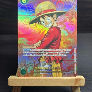 May include: A holographic trading card featuring Monkey D. Luffy from the One Piece series. The card has a colorful design with the number 6, the text "YEAH!", and the words "RED HAWK!!!!". The character is wearing a straw hat and a red shirt.