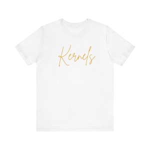 May include: White t-shirt with the word "Kernels" written in gold script.