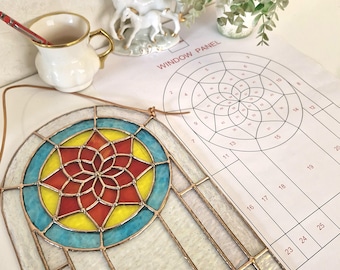 May include: A stained glass window panel with a vibrant design. The panel has a central starburst pattern in red, yellow, and orange, encircled by a blue ring. The text "WINDOW PANEL" is visible on the paper next to the panel.