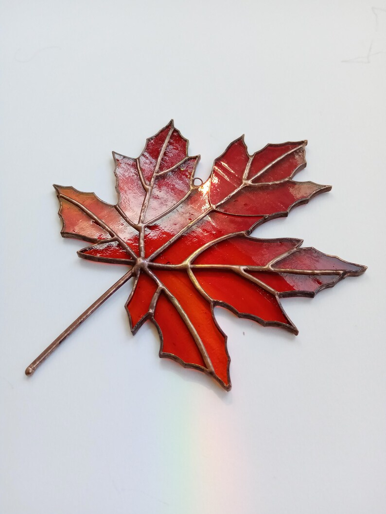 May include: A stained glass maple leaf with a copper frame. The leaf is red with orange and yellow hues.