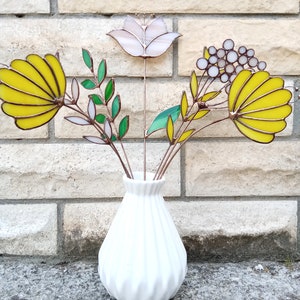 以下が含まれることがあります： テクスチャ加工された白いセラミックの花瓶に、ステンドグラスの花のブーケが活けられています。花は黄色、白、緑です。