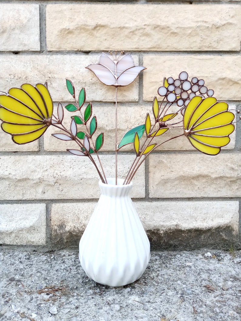 以下が含まれることがあります： テクスチャ加工された白いセラミックの花瓶に、ステンドグラスの花のブーケが活けられています。花は黄色、白、緑です。