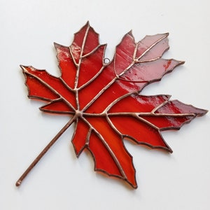 May include: A stained glass maple leaf with copper wire accents. The leaf is red with a gradient of orange and yellow.