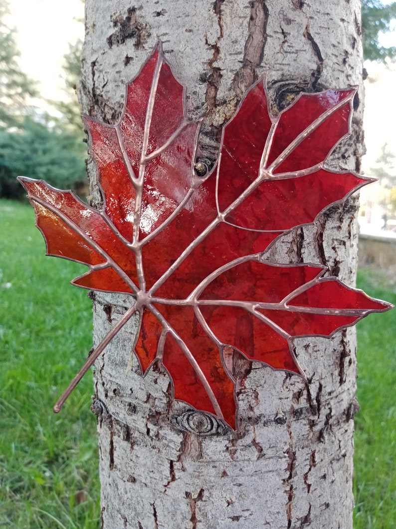 May include: A red stained glass maple leaf with copper veins, mounted on a tree trunk.