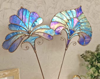 May include: Two stained glass flower garden stakes. The glass is iridescent with shades of blue, purple, and yellow. The metal stems are copper-coloured, and the stakes are in a vase. Decorative garden art.