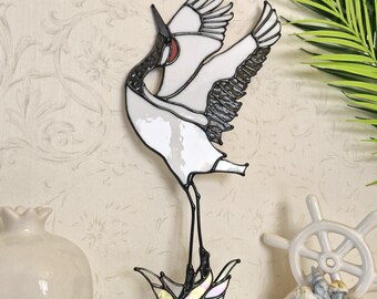 May include: A stained glass crane sculpture with outstretched wings. The bird features white, black, and red details, standing on a base of iridescent glass. The crane is a decorative item, suitable for display.