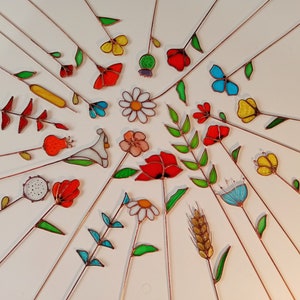 May include: A collection of colorful, stained glass flowers and leaves with copper stems arranged in a radial pattern. The flowers include daisies, tulips, and poppies in various colors, including red, yellow, and blue.