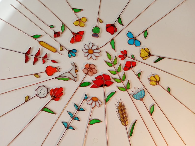 May include: A collection of colorful, stained glass flowers and leaves with copper stems arranged in a radial pattern. The flowers include daisies, tulips, and poppies in various colors, including red, yellow, and blue.