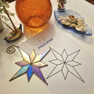 May include: A stained glass pole star with iridescent blue, purple, and gold tones. The star is hanging from a chain and is next to a printed template of a star.