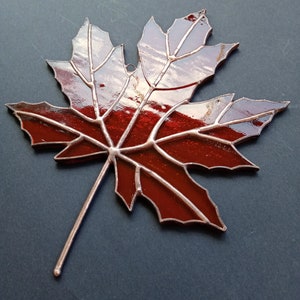 May include: A stained glass maple leaf with a copper finish. The leaf is red with a dark red outline and a copper stem.