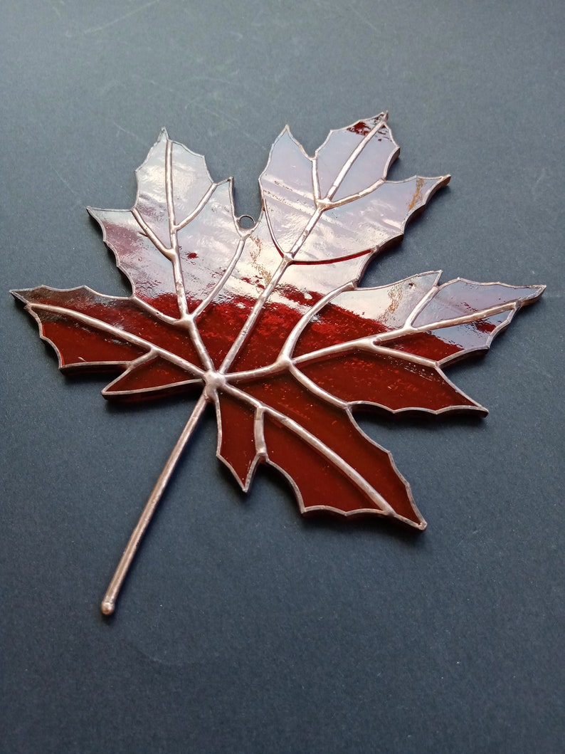 May include: A stained glass maple leaf with a copper finish. The leaf is red with a dark red outline and a copper stem.